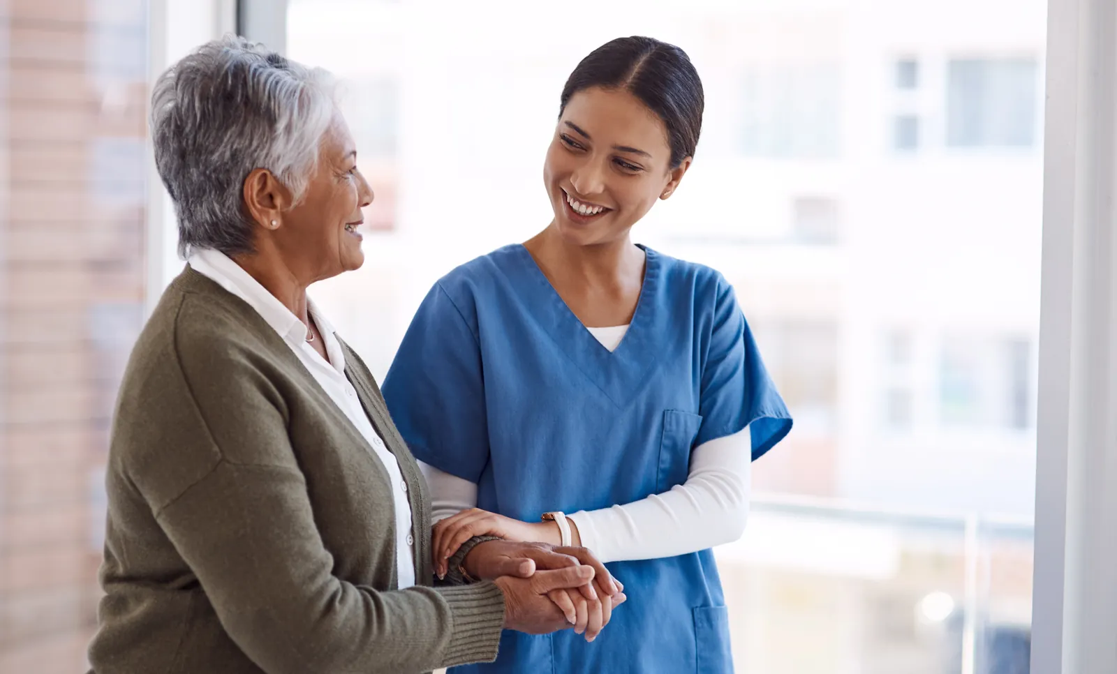 Nurse holding an older woman's hands reassuringly