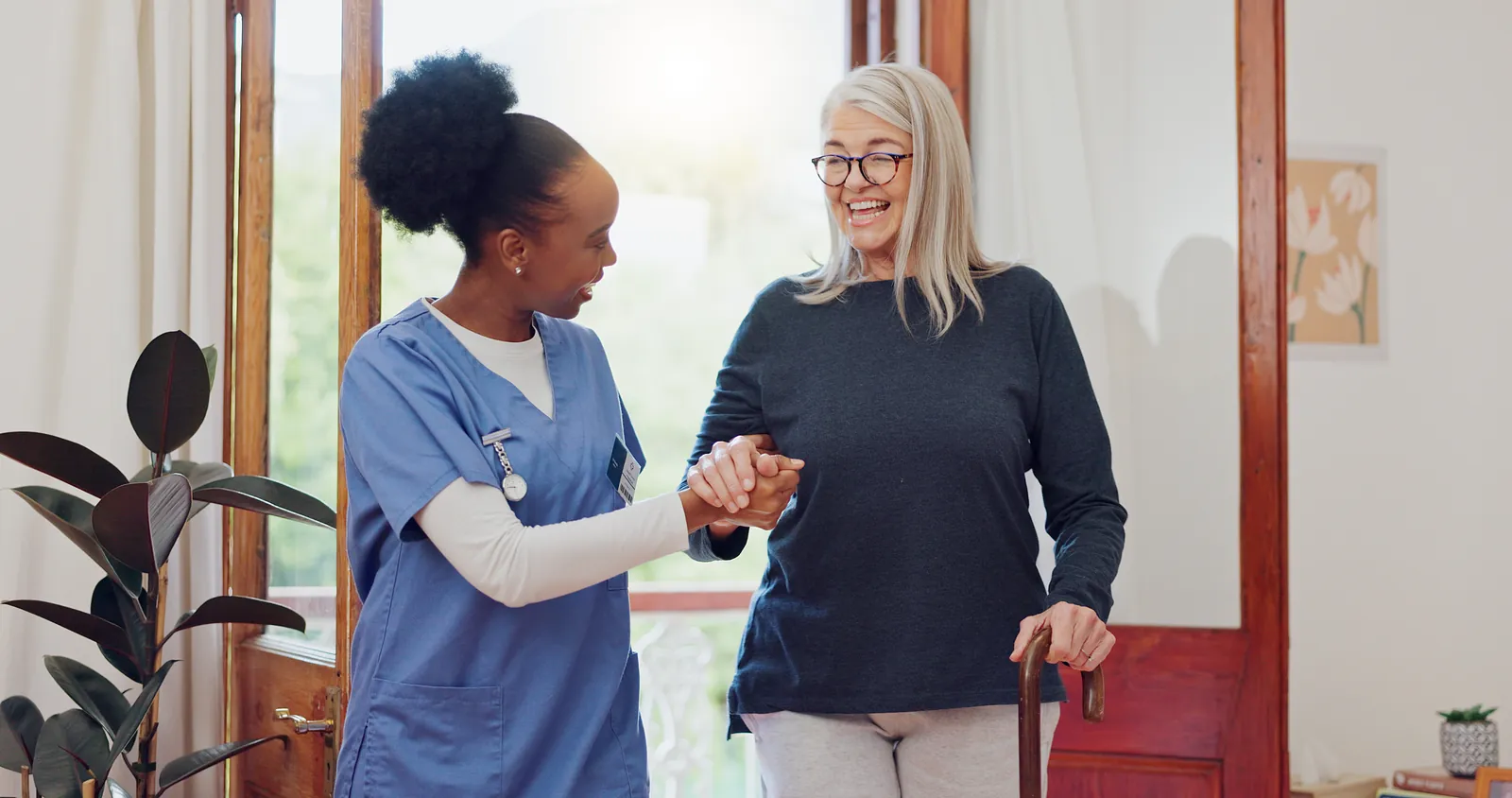 Care assistant supporting a woman walking through her hallway